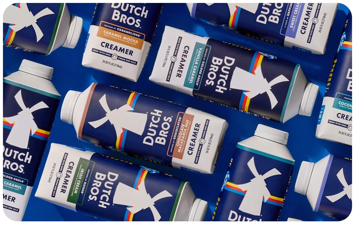 Dutch Bros coffee creamer containers in various flavors including Caramel Mocha and Vanilla arranged on blue background.