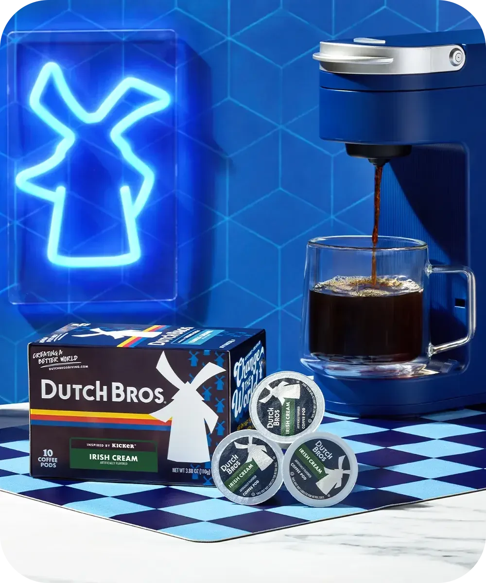 Blue Dutch Bros coffee setup with neon windmill sign, coffee machine pouring into glass mug, and Irish Cream pods.